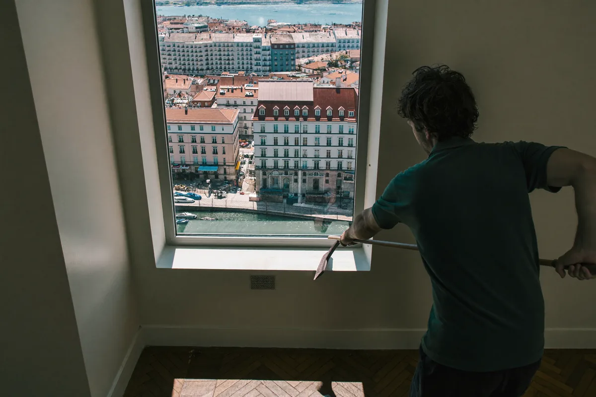 Cleaner squeegeeing a tall apartment window with Lisbon rooftops behind